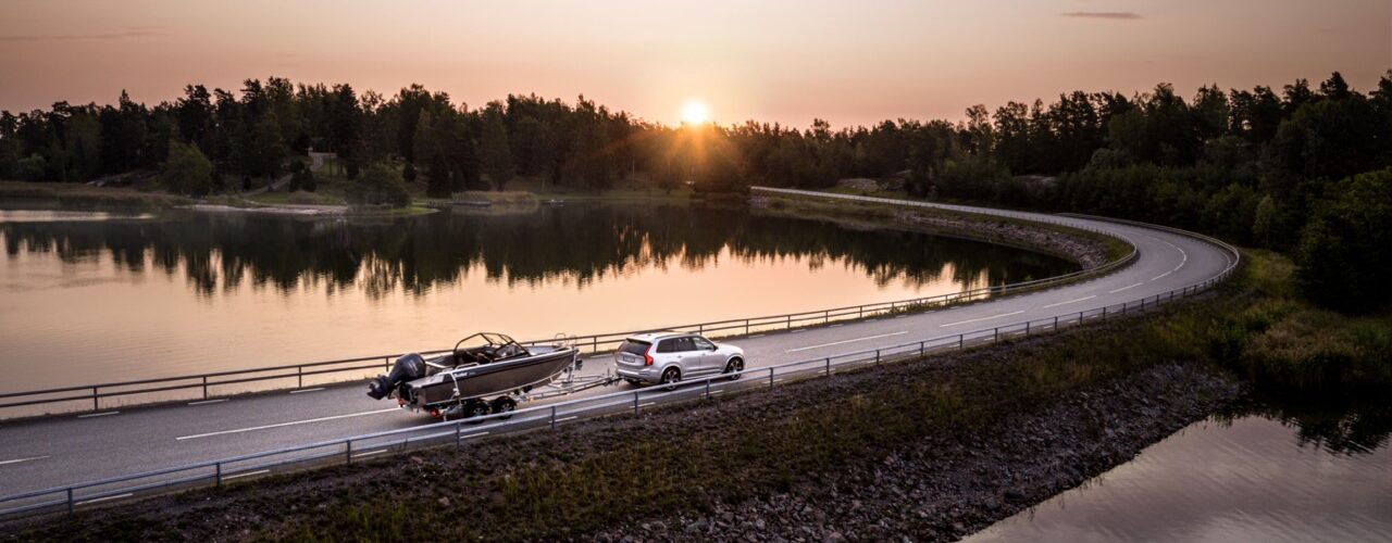 Bil med båttrailer på sommarväg vid vatten