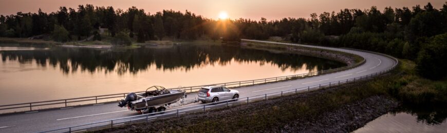 Bil med båttrailer på sommarväg vid vatten